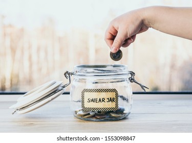Selective focus on child hand, put euro coin in swear jar. Every time child curses or swears it has to put money as punishment in jar for safe keeps. Bad habit concept. 