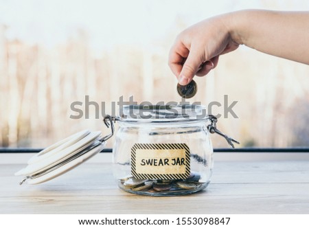 Selective focus on child hand, put euro coin in swear jar. Every time child curses or swears it has to put money as punishment in jar for safe keeps. Bad habit concept. 