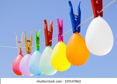 Selective focus on a colored bunch of balloons with water drops hanging on a clothesline with a blue sky as background