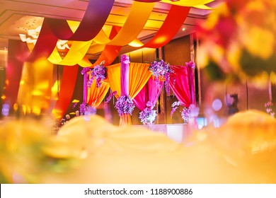 Selective focus on the colorful stage decoration with bright shade of color for bride and groom in the sangeet night of traditional indian wedding party celebration with blurry foreground