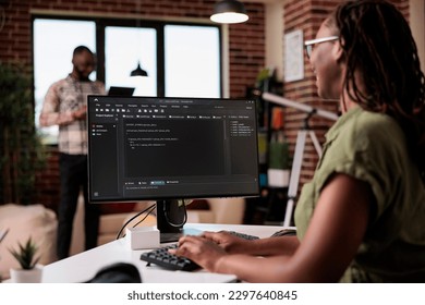 Selective focus on computer screen with programming language text of programmer working remote in home living room. African american coder developing code on pc while boyfriend is using laptop.