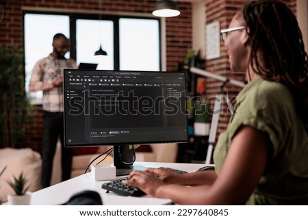 Selective focus on computer screen with programming language text of programmer working remote in home living room. African american coder developing code on pc while boyfriend is using laptop.