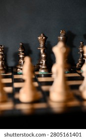 Selective focus on dark chess pieces lined up on a board against a black background, viewed from behind blurred light pieces in the foreground. Concept of tactical planning, strategy, and facing the opponent.