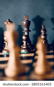 Selective focus on dark chess pieces lined up on a board against a black background, viewed from behind blurred light pieces in the foreground. Concept of tactical planning, strategy, and facing the opponent.
