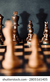Selective focus on dark chess pieces lined up on a board against a black background, viewed from behind blurred light pieces in the foreground. Concept of tactical planning, strategy, and facing the opponent.