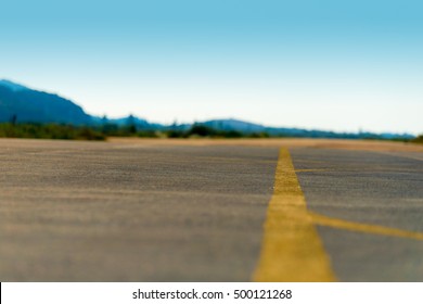 Selective focus on an empty airfield runway with yellow direction lines. Blue sky and mountains in the background.