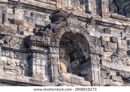 Selective focus on the face figure on the relief made of stone exposed to the sun in the Borobudur temple with blurred background, the largest temple in the world located in Indonesia.
