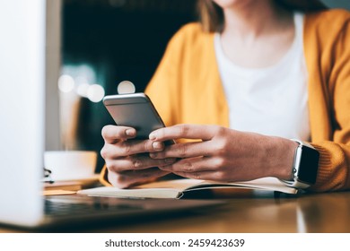 Selective focus on female hands with cellphone in hands dialing number and typing sms via application, young caucasian woman reading email from friend via smartphone device resting in cafeteria - Powered by Shutterstock