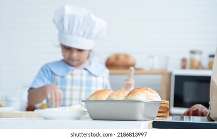 Selective focus on finished fresh homemade bread in loaf pan with little kid girl wear chef hat and apron have fun holding rolling pin to knead dough bread in kitchen at home. Child education concept - Shutterstock ID 2186813997
