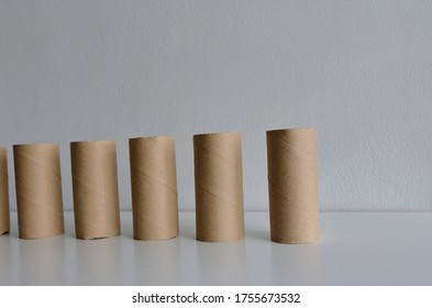 Selective focus on the first one of row of empty toilet paper rolls standing on wooden table against white cement wall under sunlight  
