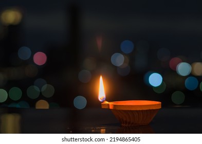 Selective focus on the flame of clay diya lamp with colorful city bokeh lights. Diwali festival concept.