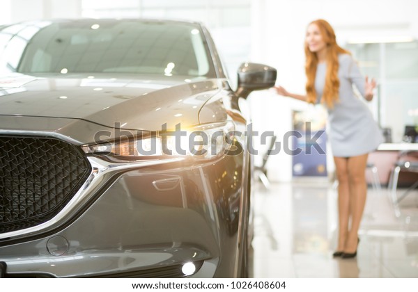 Selective focus on a flashing light of a car at the\
dealership showroom female customer examining automobile on the\
background choosing auto to buy copyspace buying shopping\
consumerism rent.