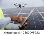 Selective focus on flying drone at solar farm with multicultural innovative specialist operating it in blurry foreground.