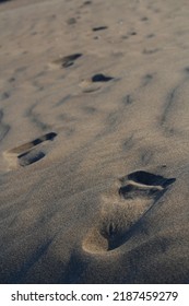 Selective focus on foreground footstep on sand and blurred footsteps on background.