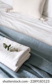 selective focus on fresh terry towels neatly folded on bed with bedclothes and blanket and decorated with eucalyptus branch, detail in bedroom interior, high angle view - Shutterstock ID 2289183123