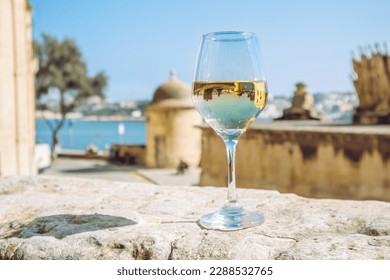 Selective focus on glass of white wine in beautiful city of Valletta in Malta. Background with blue sky and sea on sunny day. Wine tour concept. - Shutterstock ID 2288532765