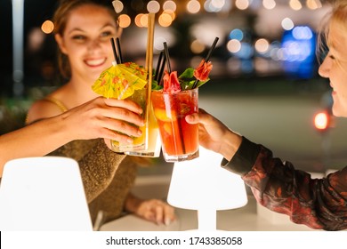 Selective focus on the glasses of three young women making a toast with cocktails on a terrace at night with the city lights on the background - Powered by Shutterstock