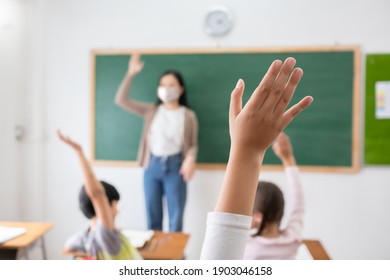 Selective focus on hand. Children or Schoolkids or students raising hands up with Asian teacher wearing protective face mask in classroom at school while covid-19 pandemic. New Normal Life concept.