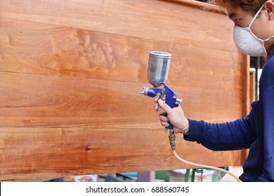 Selective Focus On Hands Of Industrial Painter With Safety Mask Painting A Wooden Furniture With Spray Gun In Home Workshop. Shallow Depth Of Field.