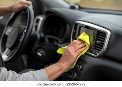 Selective focus on hands of a senior man, using a yellow microfiber cloth, applying wax, waxing, wiping and polishing the dashboard in the car interior. Car wash, detailing and valeting - Powered by Shutterstock