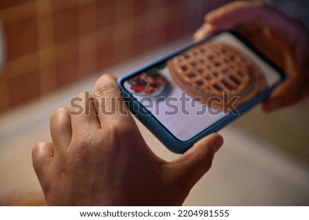 Selective focus on hands using mobile phone to photograph a homemade pie with cherries and a puff crispy crust. Smartphone in live view mode. Freshly Baked Cherry Pie with Lattice Top. Baking concept