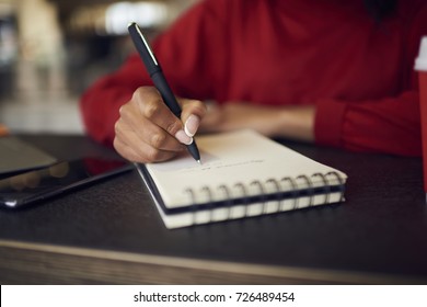 Selective focus on handwriting in spiral notebook creating to do list with targets on white page, cropped image of afro american female designer drawing sketches for project in diary with pen