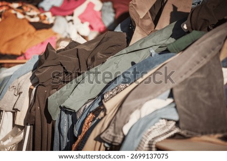 Selective focus on a heap of second hand garments at a flea market in Sabac, Serbia. Mixed fabrics convey reuse, thrift shopping, and circular fashion themes, with the background softly blurred.