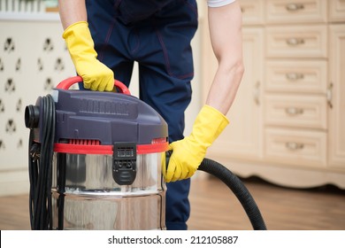 Selective focus on janitor wearing white T-shirt blue overalls and yellow rubber gloves turning off the vacuum cleaner. His working place on background