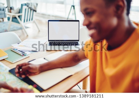 Selective focus on laptop computer with mock up screen on desktop, blurred african american hipster guy satisfied with success of online business working online via netbook and applications for blog