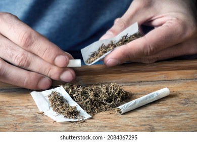 Selective focus on loose rolling tobacco with hands of a man rolling a cigarette in the background