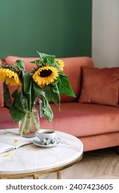 Selective focus on marble table with cup of tea, opened notebook and glass vase with yellow sunflowers against blurred living room interior. Breakfast at cozy home. Morning concept.