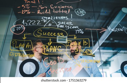 Selective focus on modern glass board with statistics planning for business marketing male colleagues discussing report information on blurred background, entrepreneurs creating strategy indoors - Powered by Shutterstock