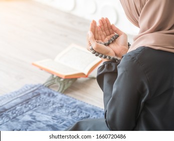 Selective focus on Moslem pray, praying hands to Allah with misbaha beads of Muslim lady with blurry quran resting on table stand beside blue mat.