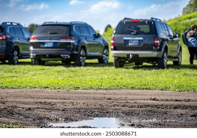 Selective focus on mud and torn up grass in the foreground of a dirt parking lot