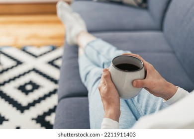 Selective Focus On Mug With Hot Drink In Female Hands At Morning, Rest And Enjoy On Sofa In Living Room With Blurred Background, Cropped Shot