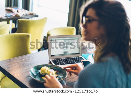 Selective focus on opened modern laptop computer with wireless internet connection.Young woman freelancer eating delicious food having dinner in cafe interior during work's break