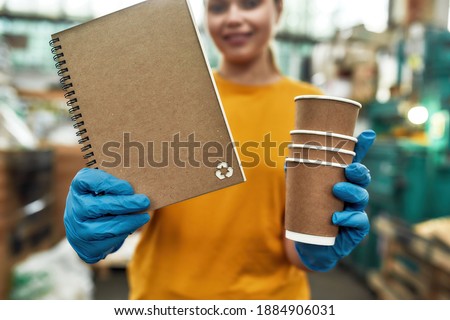 Selective focus on paper notebook produced from recycled cups held by girl working on waste station, cropped. Garbage sorting and recycling concept