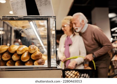 Selective focus on a pastry in show window with an old couple choosing groceries at bakery department in supermarket. - Powered by Shutterstock