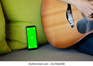 Selective focus on phone with greenscreen of chromakey mockup with tracking markers near woman learning to play guitar. Green screen and chroma key with copy space. Online guitar courses. - Powered by Shutterstock