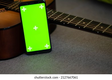 Selective Focus On Phone With Greenscreen Of Chromakey Mockup With Tracking Markers Near The Guitar With Copy Space. Green Screen And Chroma Key. Online Guitar Courses.