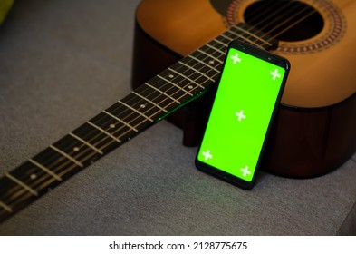 Selective Focus On Phone With Greenscreen Of Chromakey Mockup With Tracking Markers Near The Guitar With Copy Space. Green Screen And Chroma Key. Online Guitar Courses.