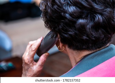 Selective Focus On The Phone. The Phone Is In The Hand Of A Senior Woman With Short Black Hair And She Is Currently Talking. The Picture Is From The Back.