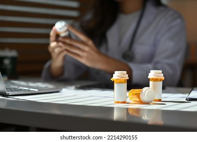 Selective Focus On Pill Bottles With Empty Label And Female Pharmacist Checking Pill Bottles And Reading Drug Labels As The Background.