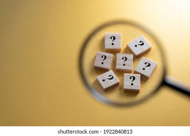 Selective focus on Question Mark symbol on a wooden tiles using magnifying glass against yellow background. Concept of Q and A, questions and faq