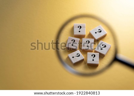 Selective focus on Question Mark symbol on a wooden tiles using magnifying glass against yellow background. Concept of Q and A, questions and faq