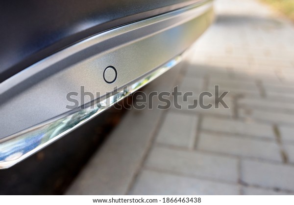 Selective focus on rear bumper left side\
parking sensor at back of luxurious car bumper close up on light\
blurred with sun flare background with\
copyspace.