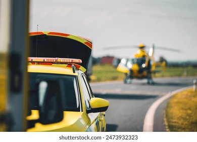 Selective focus on red light flasher on roof of ambulance car of emergency medical service against helicopter landing on road. Themes rescue, urgency and health care.	