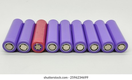 Selective focus on a red lithium battery among a stack of purple lithium batteries on a white background