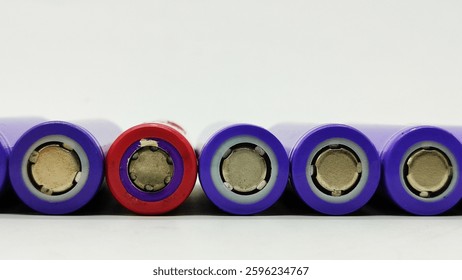 Selective focus on a red lithium battery among a stack of purple lithium batteries on a white background