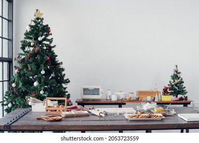 Selective focus on round gingerbread cookies are baked on plate with gingerbread man molds, raw ingredients, kitchenware on wooden table at home kitchen decorated with Christmas trees